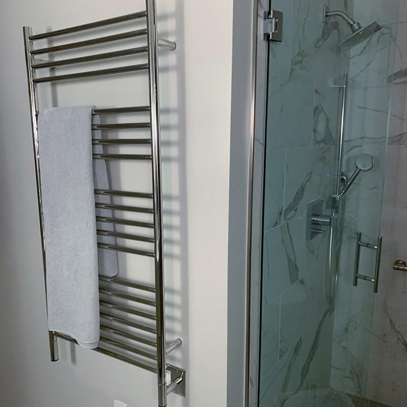 Amba Jeeves Model D Straight 20 Bar Hardwired Towel Warmer in Polished Stainless Mounted Beside a Glass Door